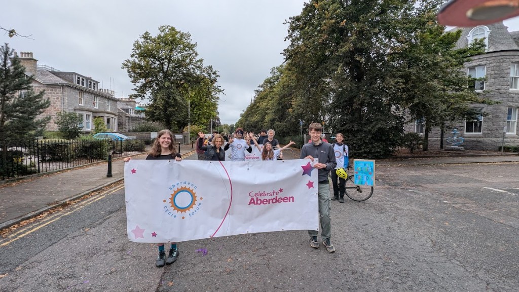 Aberdeen Cycle Forum banner with members smiling behind it, waiting to start the parade.